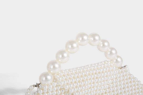 Small structured triangle clutch bag covered in glossy pearl beads with an arched pearl top handle and silver snap closure