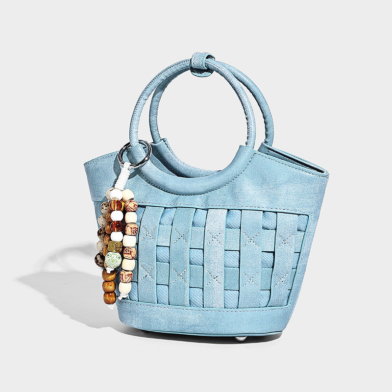 Small structured woven bucket bag with round top handle, beaded charm, and detachable shoulder strap in leather-look finish