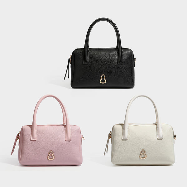 Small structured pillow satchel bag with pebbled leather-look finish, dual rolled top handles, gold-tone gourd emblem, and