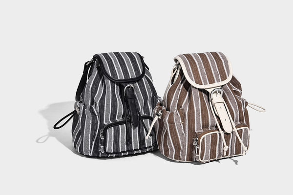 Weicher Rucksack aus gewebtem Material mit vertikalen Streifen, Überschlag, Kordelzug, vorderer Reißverschlusstasche, weißen Besätzen und Trägern in Lederoptik, Detailansicht