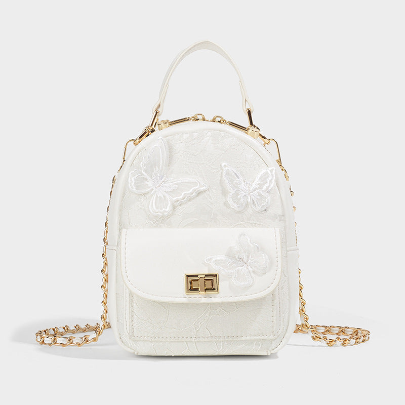 Structured mini backpack handbag with butterfly embroidery, gold-tone chain strap, and turn-lock front flap pocket, detail