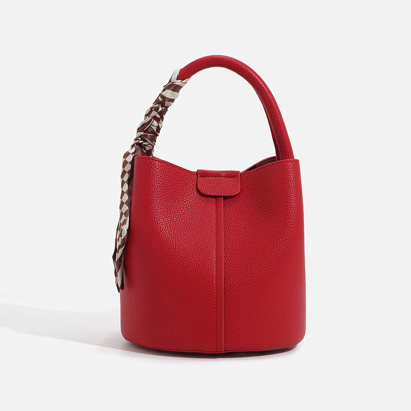 Pebbled leather-look bucket bag with checkered scarf-wrapped top handle, flap tab closure, gold-tone hardware, and matching