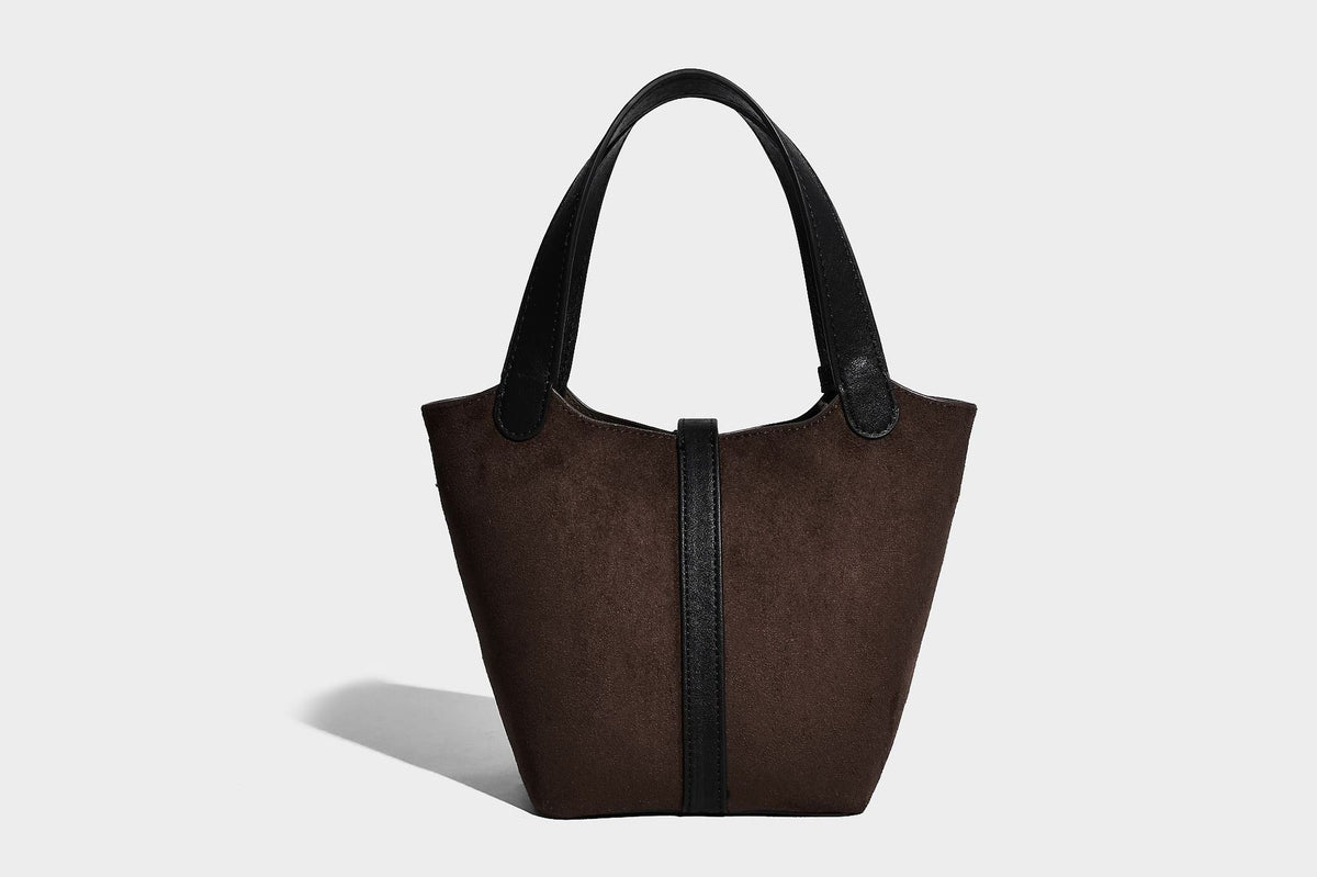 Small structured trapezoid tote bag in matte suede-look finish with black contrast trim, gold-tone front clasp, tassel charm