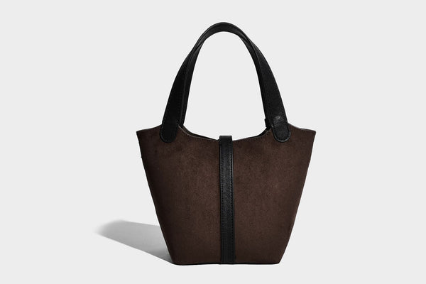 Small structured trapezoid tote bag in matte suede-look finish with black contrast trim, gold-tone front clasp, tassel charm