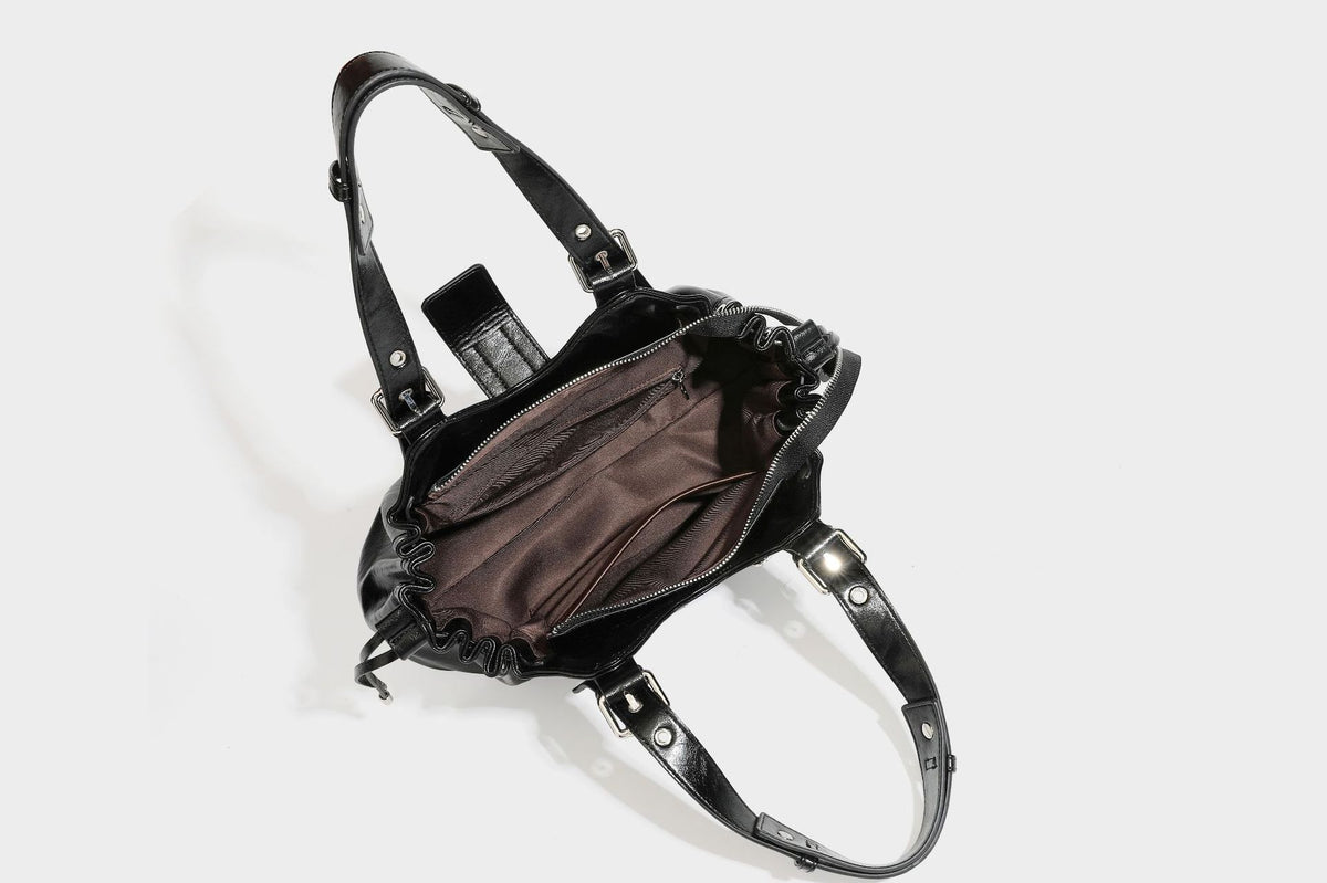 Large black glossy leather-look tote bag with silver buckle straps, eyelet grommet panels, drawstring side gathers, and