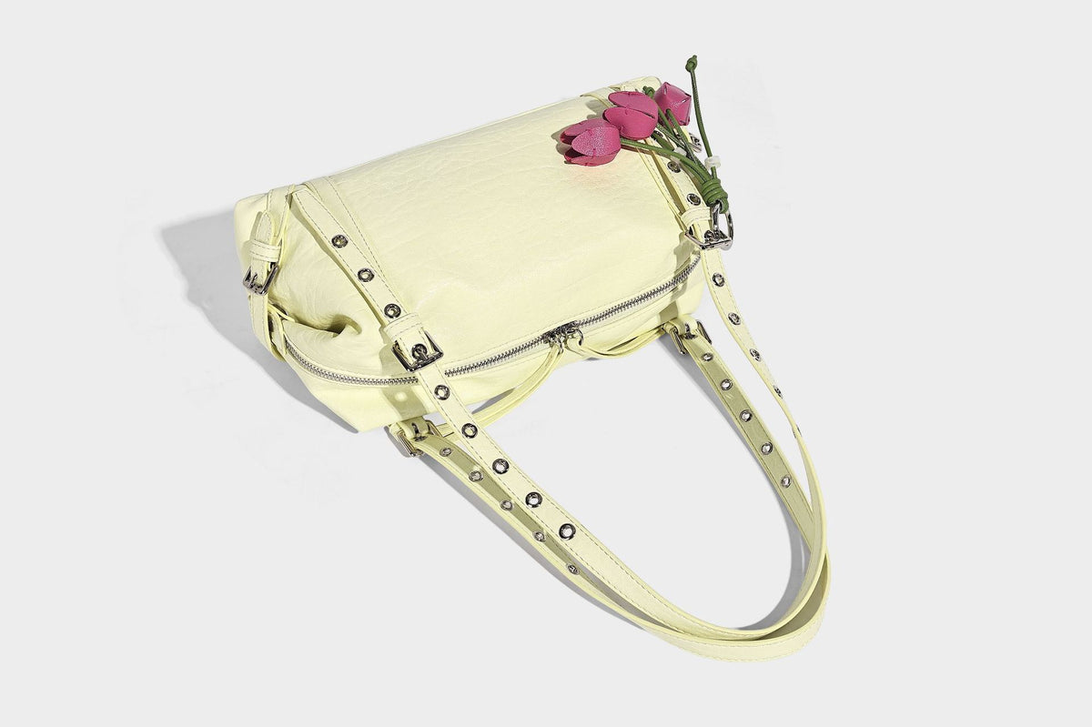 Pale yellow leather-look barrel bag with silver grommet-studded shoulder straps, top zip closure, and pink tulip floral