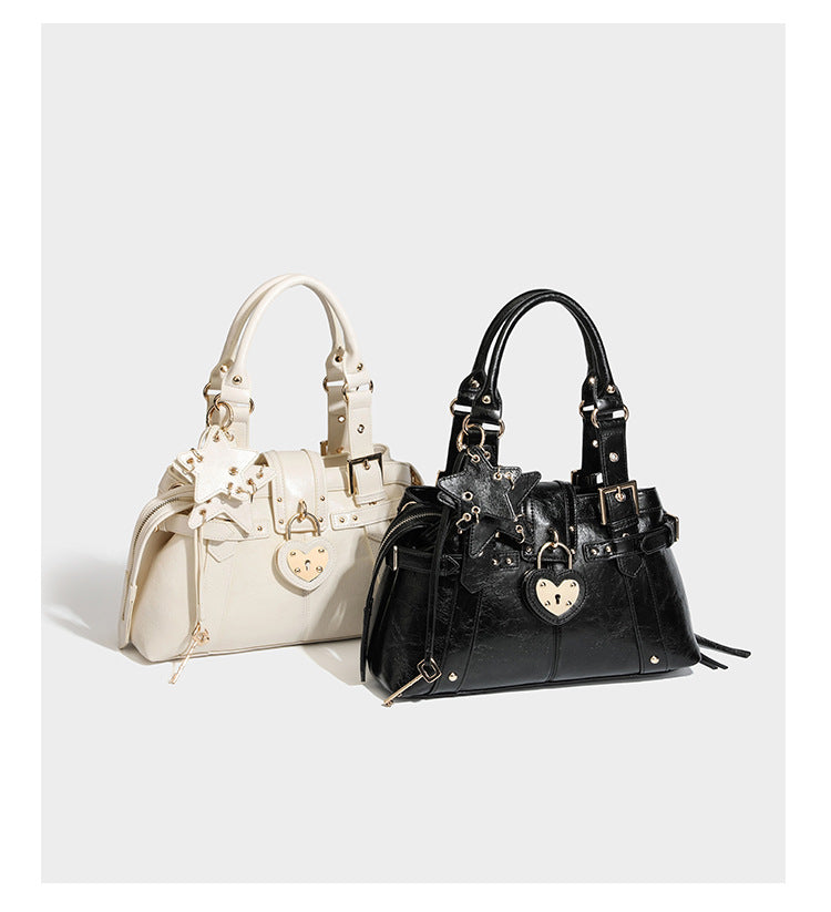 Structured leather-look satchel bag with heart padlock charm, star charm, gold-tone buckle hardware, dual top handles, and