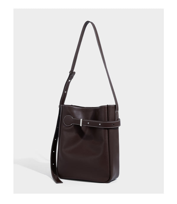 Structured dark brown leather-look bucket bag with white contrast stitching, front wraparound belt buckle strap, and long