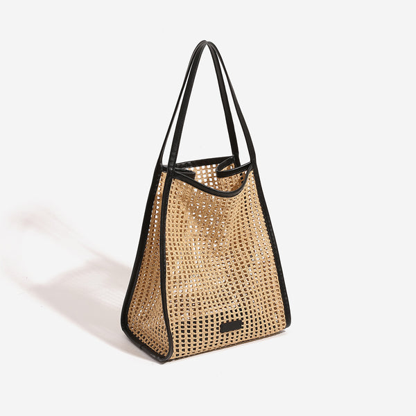 Tan open-weave raffia tote bag with black leather-look trim and long black shoulder straps, trapezoid silhouette, detail view