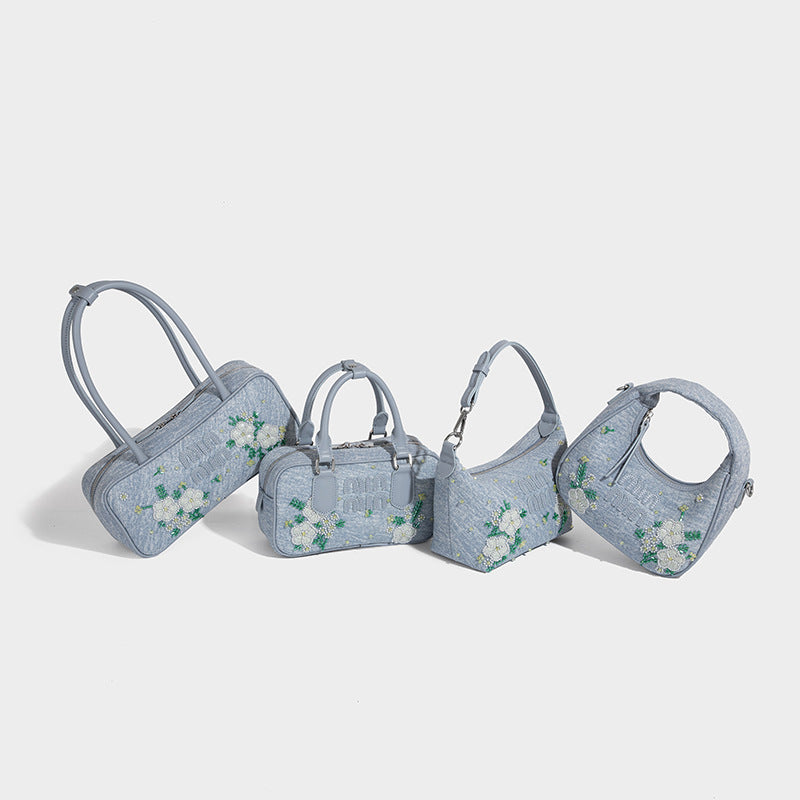 Small structured light blue denim-texture bowling bag with white floral bead embroidery, dual rounded top handles, and