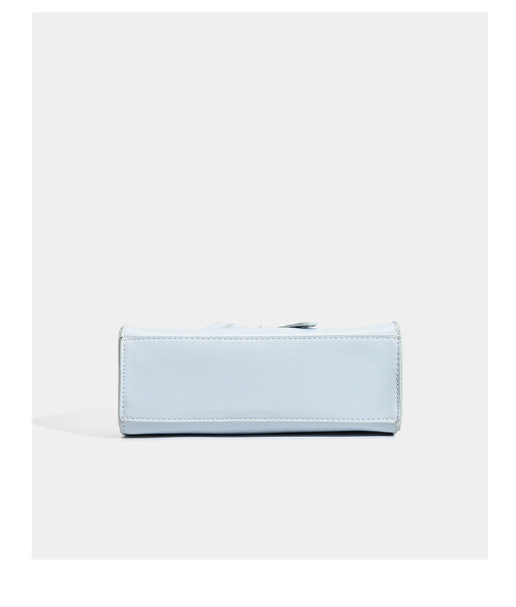 Small structured trapezoid mini top-handle bag with front belt-knot buckle detail and glossy leather-look finish, detail view
