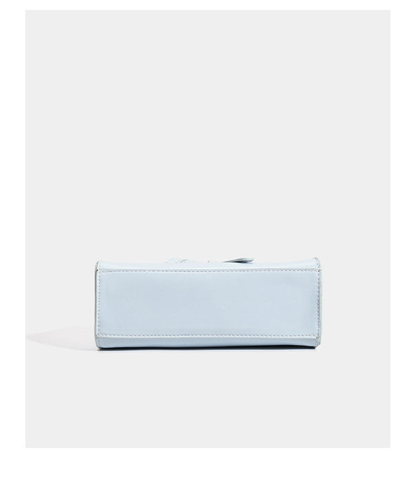 Small structured trapezoid mini top-handle bag with front belt-knot buckle detail and glossy leather-look finish, detail view