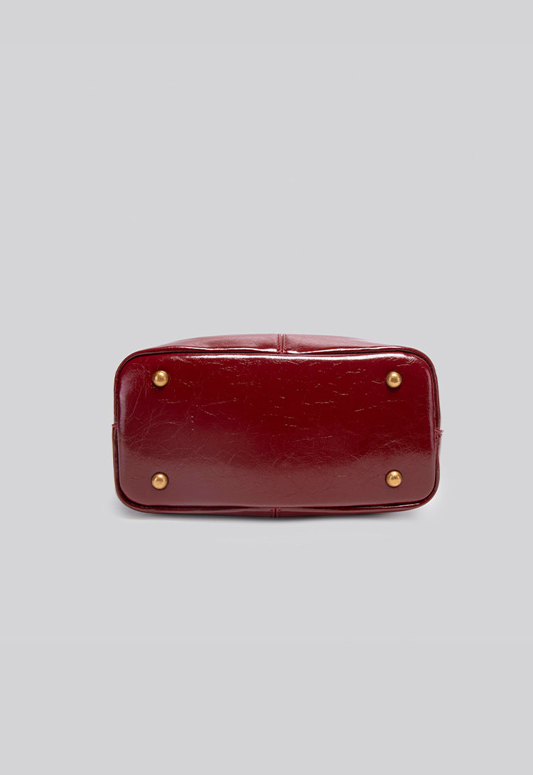 Structured crinkle-gloss top-handle satchel in deep burgundy with antique gold lock charm and detachable shoulder strap