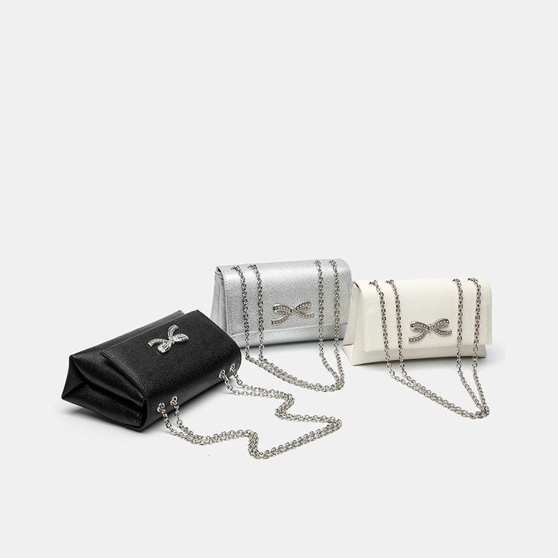 Structured rectangular flap crossbody bag with rhinestone bow and silver chain strap in pebbled finish, detail view 2