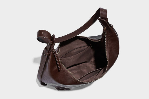 Lässig fallende, sichelförmige Hobo-Schultertasche in glatter dunkelbrauner Lederoptik mit Logo-Anhänger in Goldoptik und verstellbarem Schulterriemen