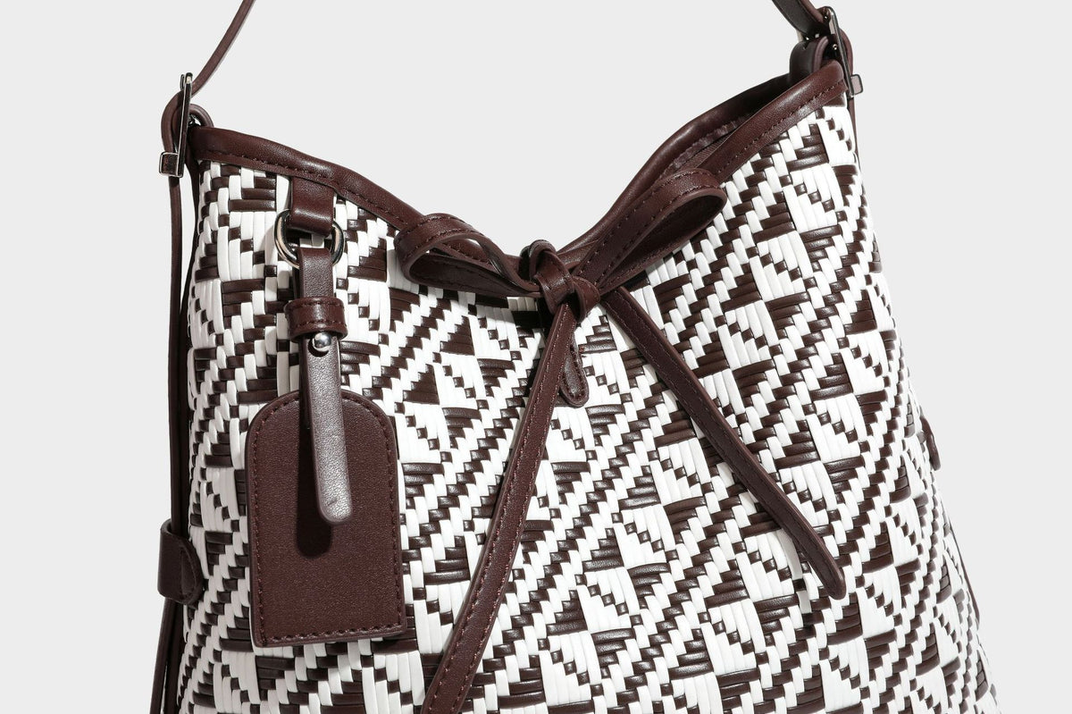 Woven geometric bucket shoulder bag in white and dark brown two-tone pattern with leather-look trim and drawstring top
