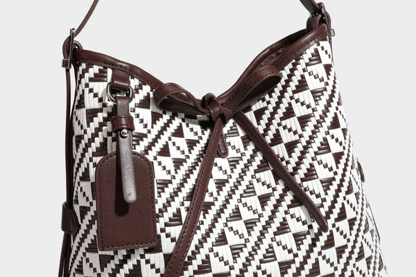 Woven geometric bucket shoulder bag in white and dark brown two-tone pattern with leather-look trim and drawstring top