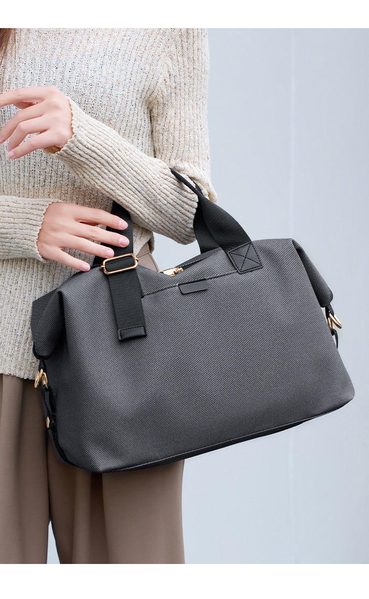 Structured woven duffel bag with dual tan webbing handles, detachable shoulder strap, top zip closure, and gold-tone