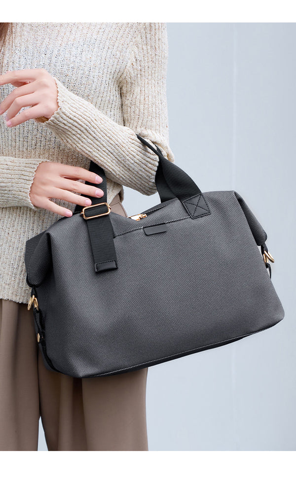Structured woven duffel bag with dual tan webbing handles, detachable shoulder strap, top zip closure, and gold-tone