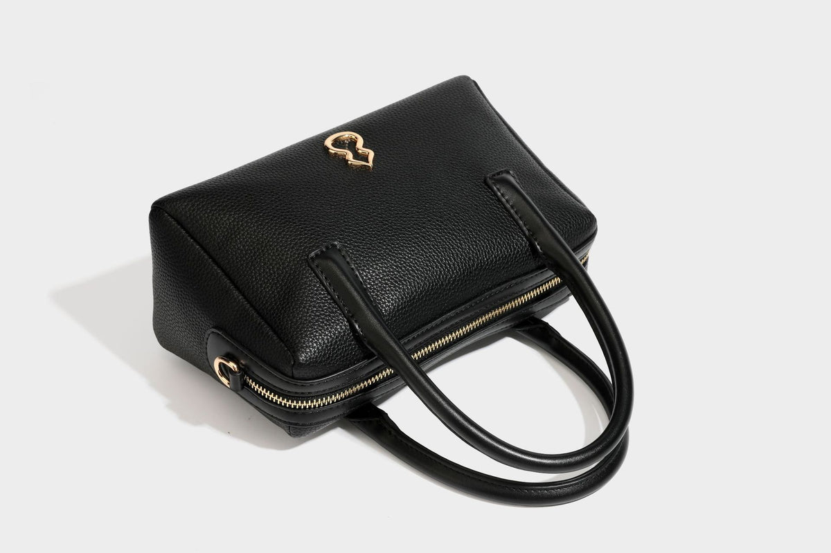 Small structured pillow satchel bag with pebbled leather-look finish, dual rolled top handles, gold-tone gourd emblem, and
