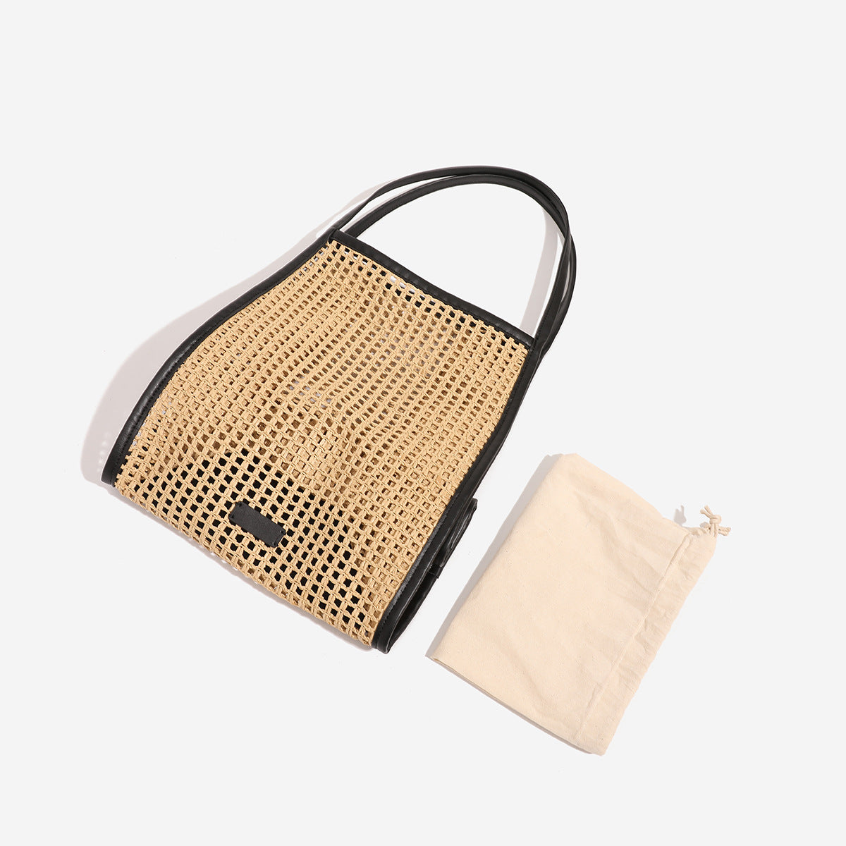 Tan open-weave raffia tote bag with black leather-look trim and long black shoulder straps, trapezoid silhouette, detail view