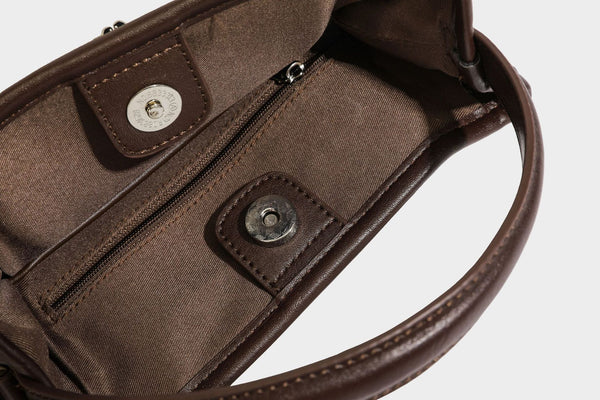 Small structured beige canvas top-handle bag with dark brown leather-look trim, silver turn-lock hardware, and detachable