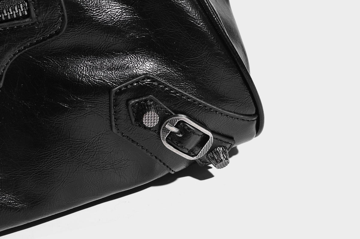 Längliche Schultertasche in Zylinderform mit glänzender Lederoptik, silberfarbenen Nietenbeschlägen, seitlichen Quasten und mehreren außenliegenden Reißverschlüssen
