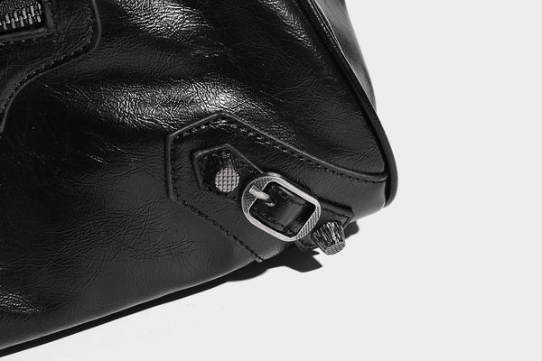 Längliche Schultertasche in Zylinderform mit glänzender Lederoptik, silberfarbenen Nietenbeschlägen, seitlichen Quasten und mehreren außenliegenden Reißverschlüssen