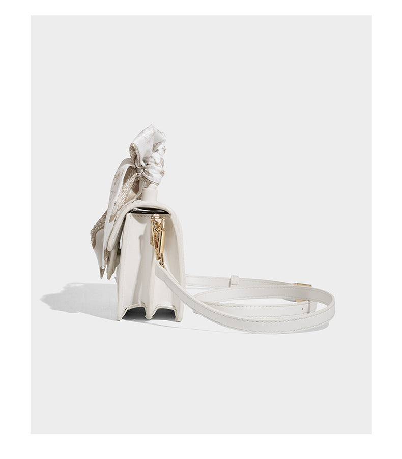 Small structured white flap bag with butterfly embroidery, flower-shaped turn-lock clasp, braided top handle with scarf bow