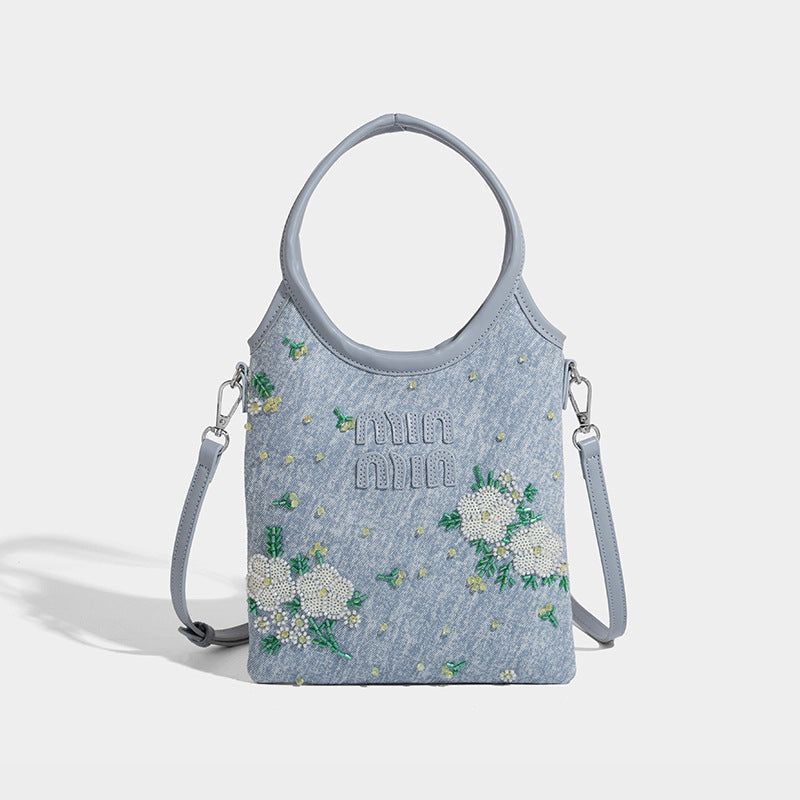Kleine hellblaue Mini-Tote-Bag aus Stoff mit weißer Blumenverzierung aus Perlen, runden Tragegriffen, silberfarbenen Metallelementen und