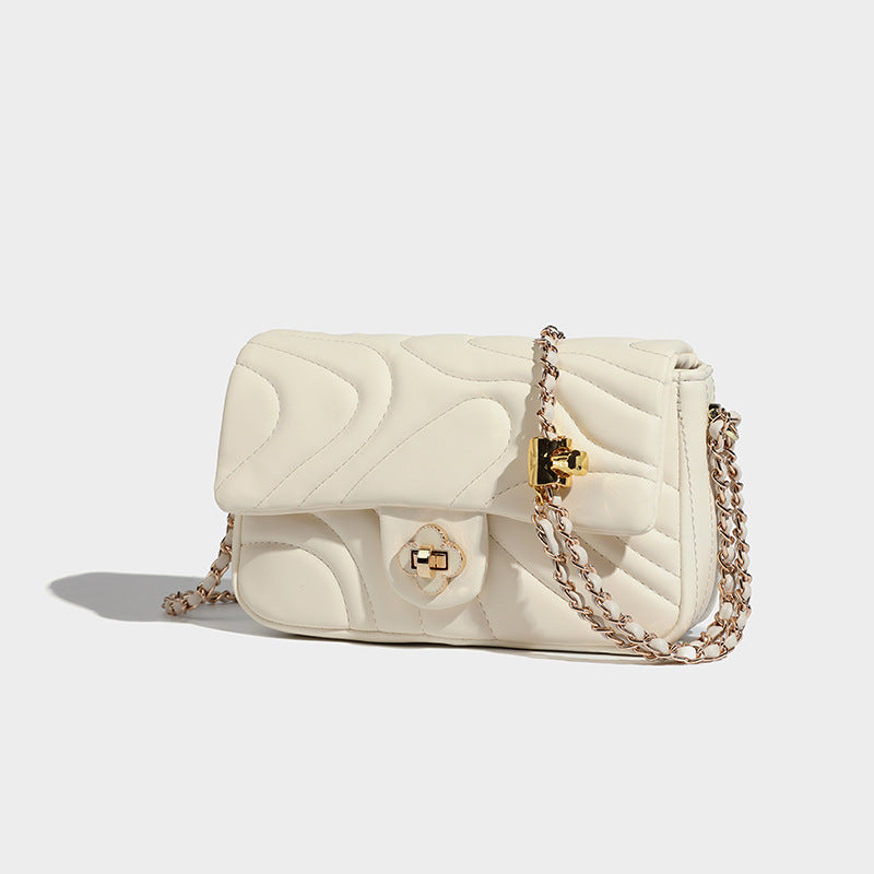 Compact cream quilted flap crossbody bag with wave stitching, gold-tone chain strap, and four-petal turn-lock clasp, detail