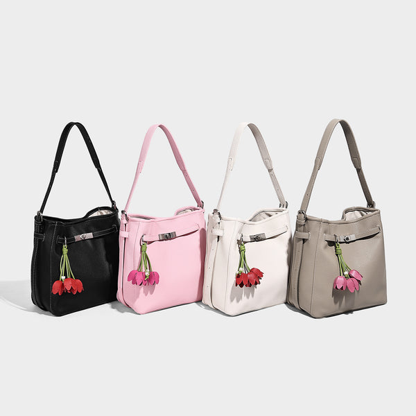 Soft-structured pebbled bucket shoulder bag with front turn-lock strap detail, adjustable strap, and hanging floral tassel