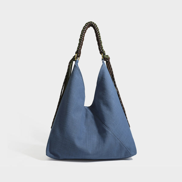 Soft slouchy cream canvas shoulder tote with braided brown and green cord handle, gold-tone ring hardware, and tassel trim