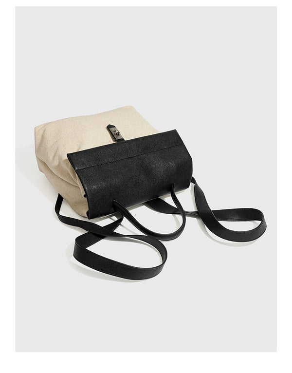 Strukturierter beigefarbener Rucksack aus gewebtem Canvas mit schwarzer Klappe in Lederoptik, Drehverschluss, Tragegriff und flachem Schulter