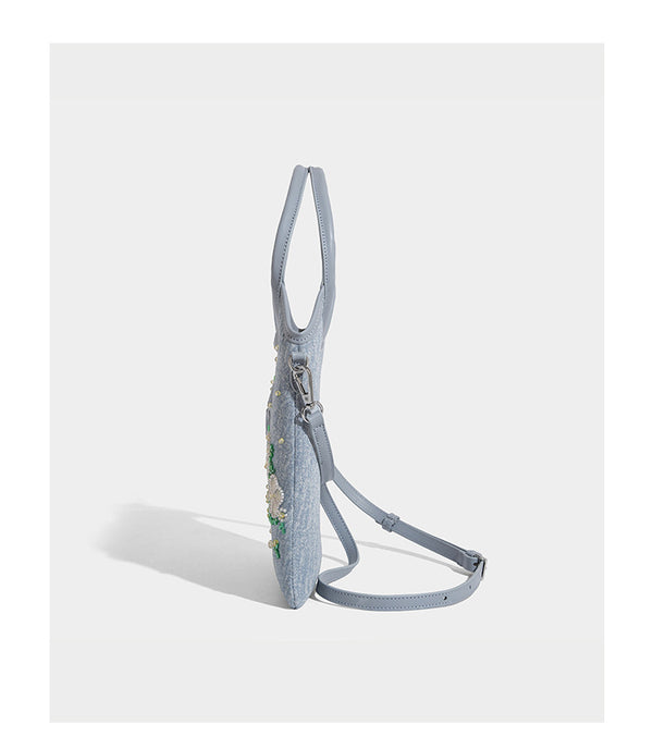 Kleine hellblaue Mini-Tote-Bag aus Stoff mit weißer Perlenblumenverzierung, runden Henkeln, silberfarbenen Beschlägen und