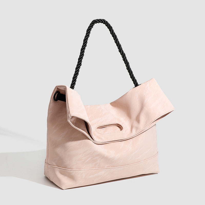 Large blush pink tote bag with twisted black rope handle and oval cutout carry slot, crinkled textured finish, detail view 2
