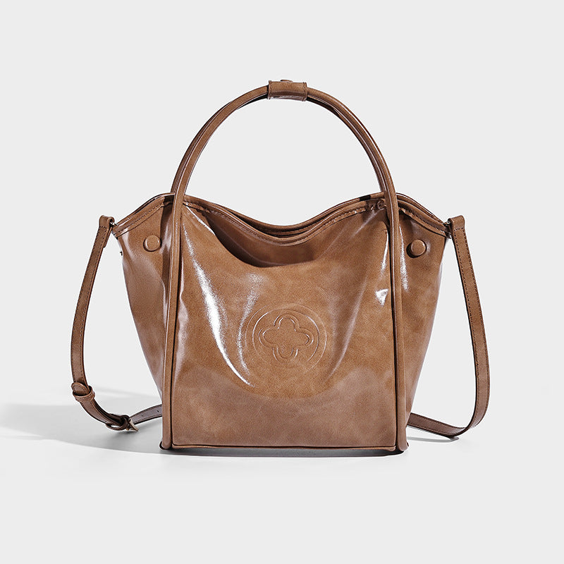 Glossy leather-look structured tote bag with rounded top handles, detachable shoulder strap, embossed front emblem, and side