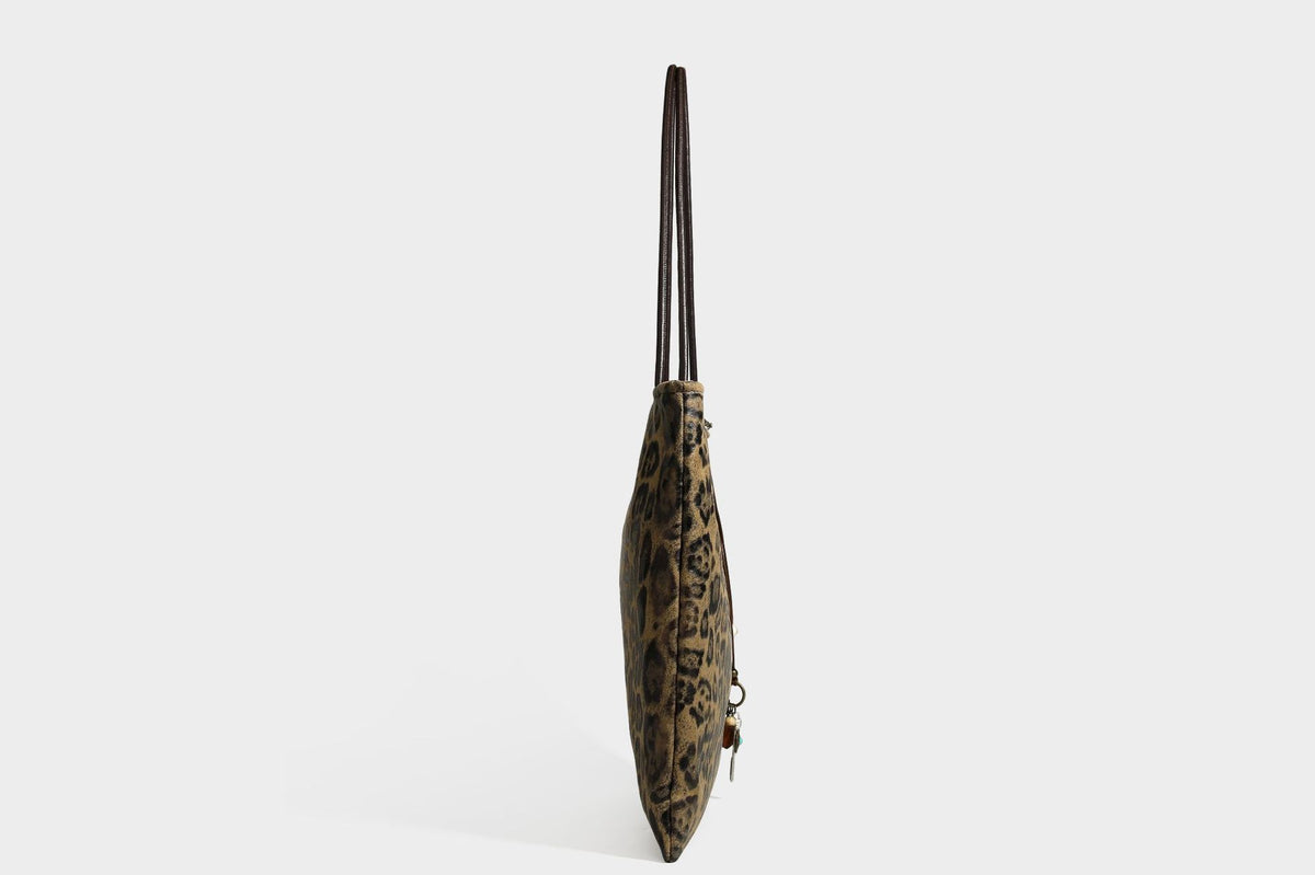 Large leopard print shoulder tote bag in tan and brown with slim dark straps and dangling beaded charm hardware, detail view