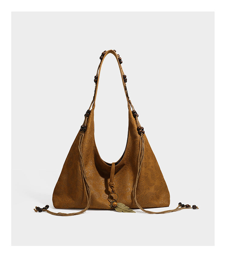 Slouchy boho hobo shoulder bag in embossed brown suede-look finish with beaded strap, cord tassels, and brass-tone leaf