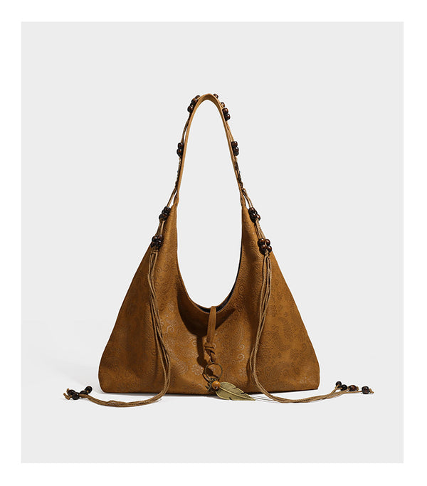 Slouchy boho hobo shoulder bag in embossed brown suede-look finish with beaded strap, cord tassels, and brass-tone leaf