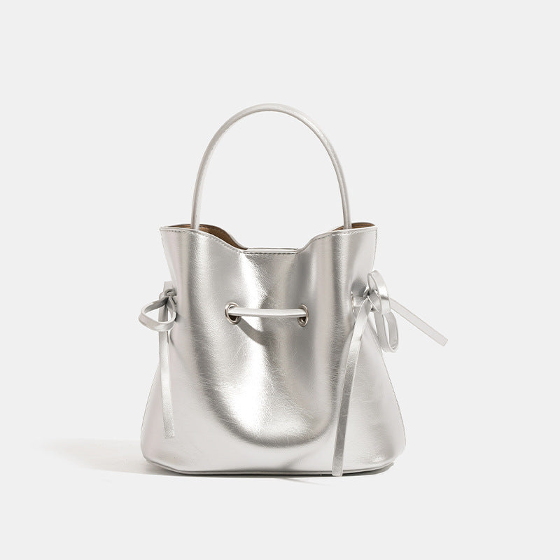 Compact glossy leather-look bucket bag with drawstring bow-tie closure, rounded top handle, and silver-tone grommet hardware