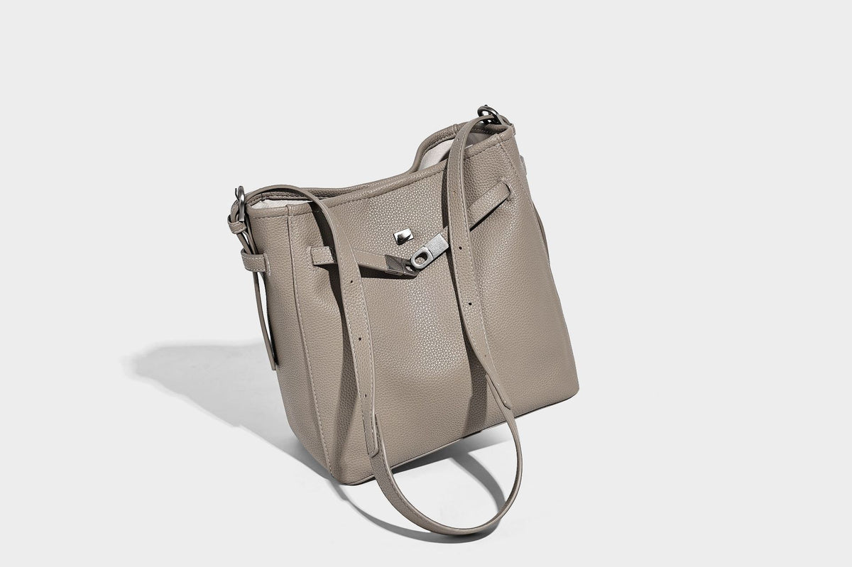 Soft-structured pebbled bucket shoulder bag with front turn-lock strap detail, adjustable strap, and hanging floral tassel