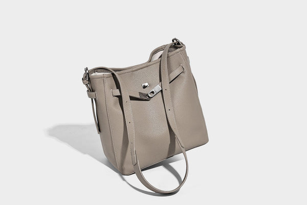 Soft-structured pebbled bucket shoulder bag with front turn-lock strap detail, adjustable strap, and hanging floral tassel