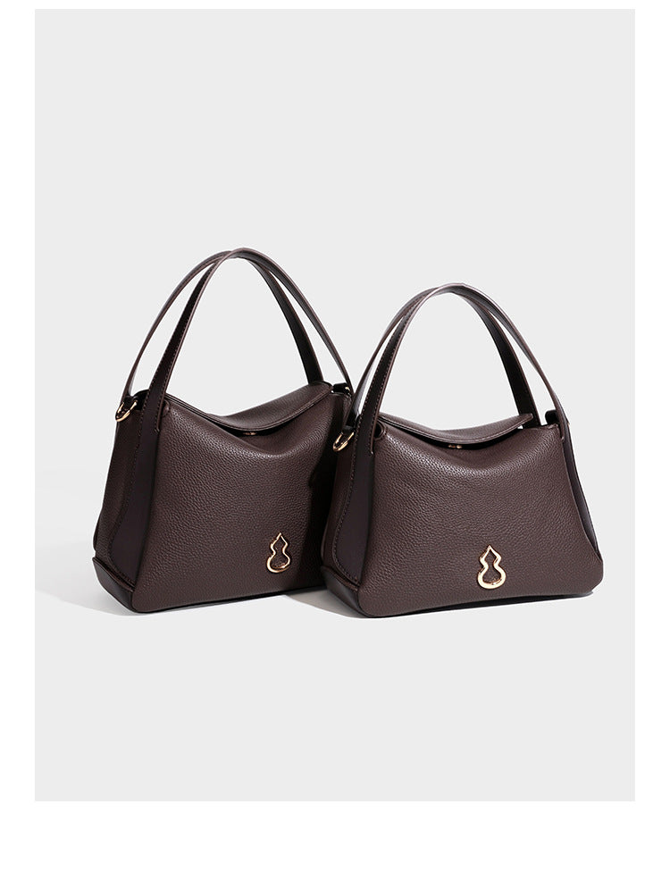 Structured pebbled leather-look shoulder bag with flap top, gold-tone emblem hardware, dual top handles, and detachable