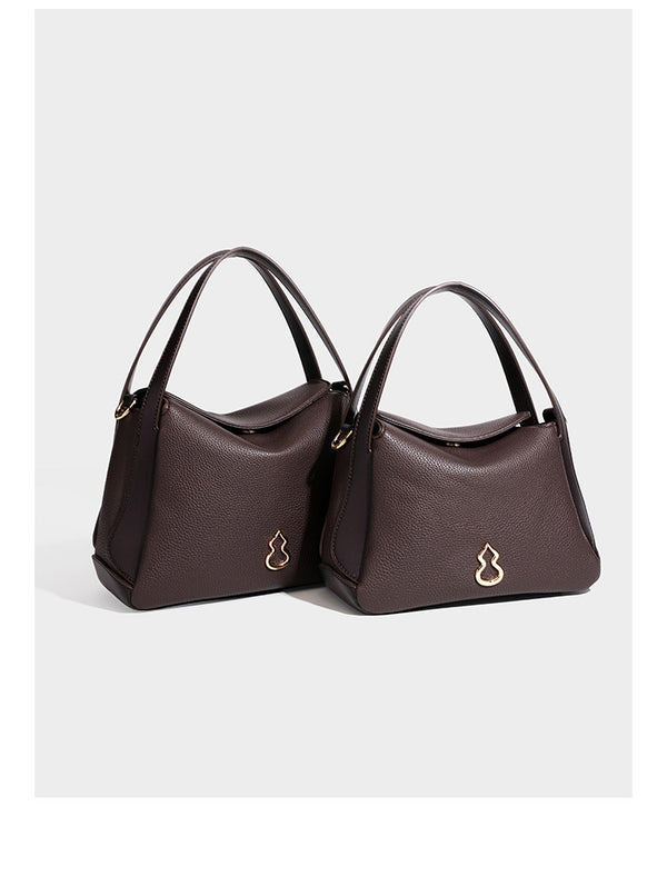Structured pebbled leather-look shoulder bag with flap top, gold-tone emblem hardware, dual top handles, and detachable