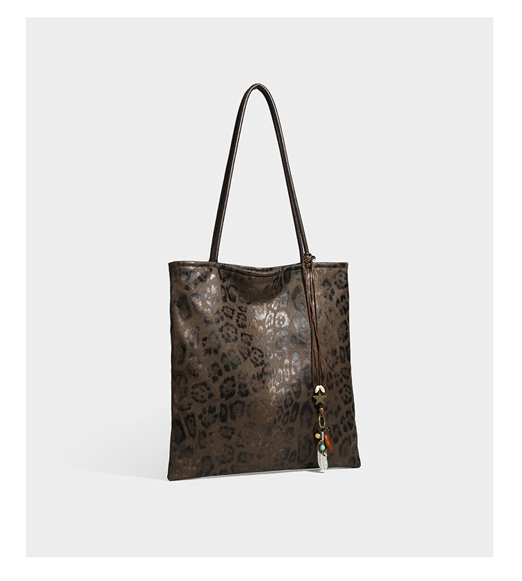 Large leopard print shoulder tote bag in tan and brown with slim dark straps and dangling beaded charm hardware, detail view