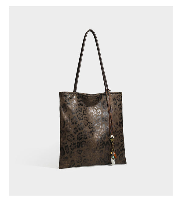 Large leopard print shoulder tote bag in tan and brown with slim dark straps and dangling beaded charm hardware, detail view