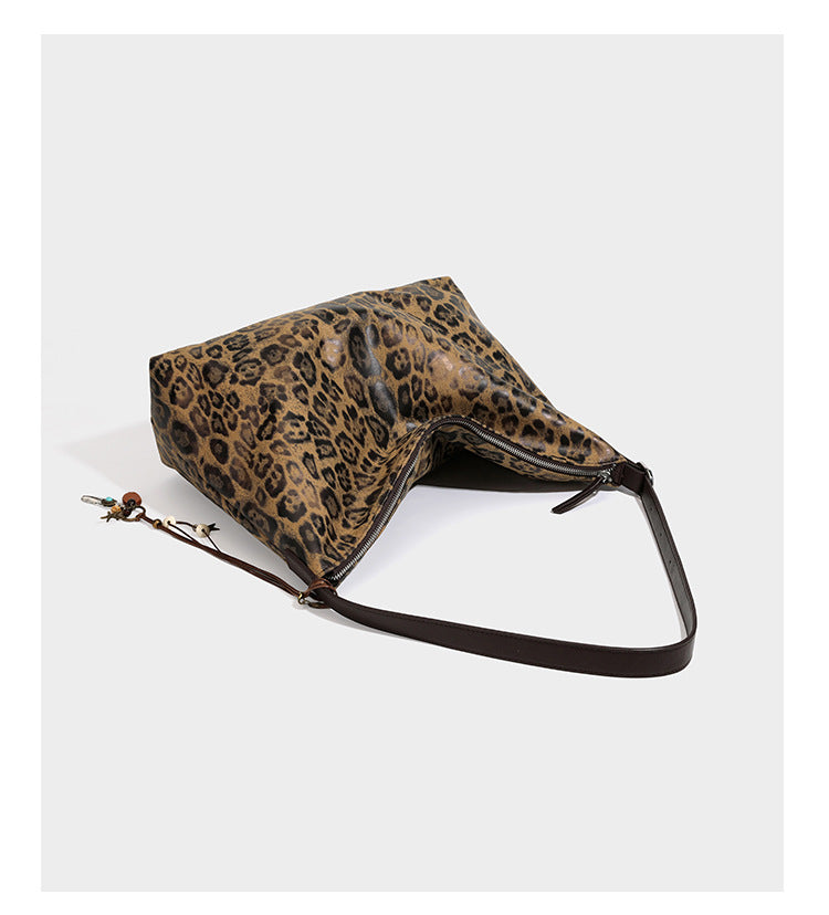 Slouchy leopard print hobo shoulder bag with glossy coated finish, top zipper closure, dark brown trim, and dangling charm