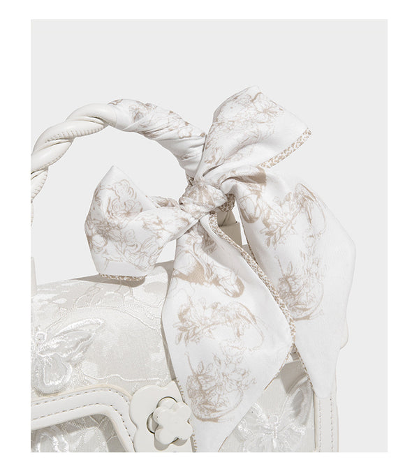 Small structured white flap bag with butterfly embroidery, flower-shaped turn-lock clasp, braided top handle with scarf bow