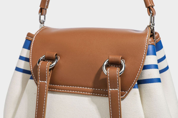 Cream canvas bucket bag with blue horizontal stripes, tan leather-look flap and trim, drawstring closure, silver-tone, detail